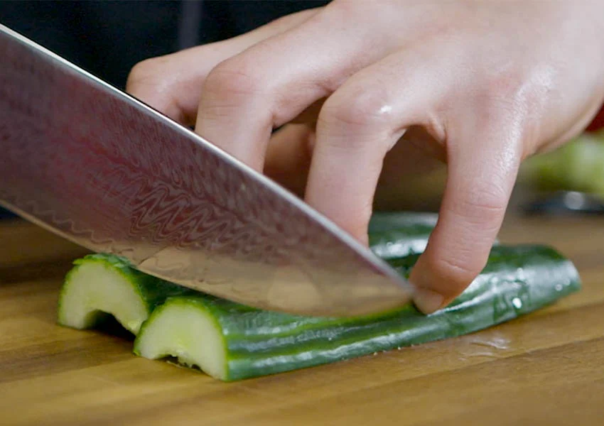 An image of someone using the claw grip to properly cut some cucumbers. How to use a knife safely? This dude definitely knows!
